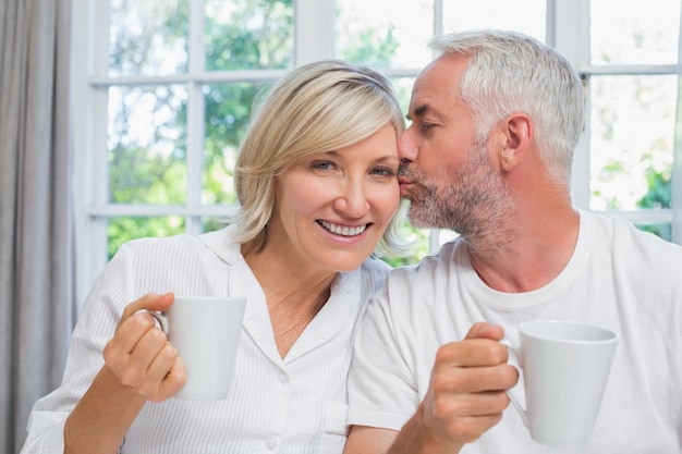 Uomo maturo che bacia donna mentre mangia caffè a letto