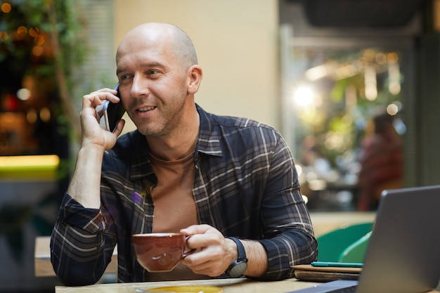 Uomo maturo che beve caffè e parla al telefono cellulare mentre si lavora al bar