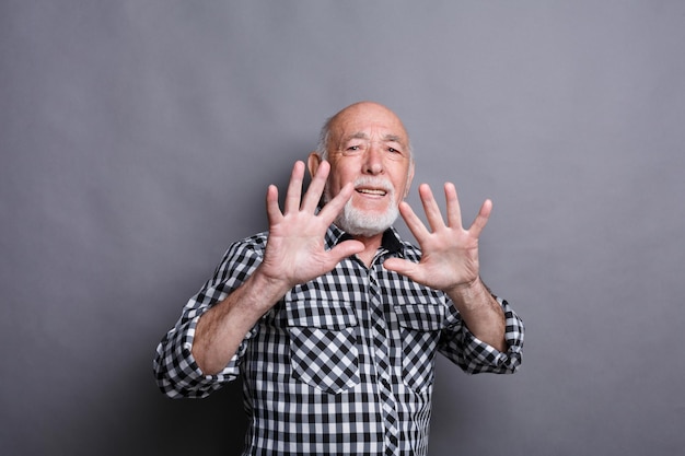 Uomo maturo che esprime disgusto sul viso e fa un gesto di obiezione con le mani, facendo smorfie alla telecamera, sfondo grigio studio. Emozioni negative, copia spazio