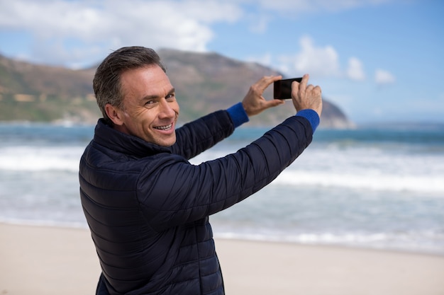 Uomo maturo che fotografa paesaggio facendo uso del telefono cellulare sulla spiaggia