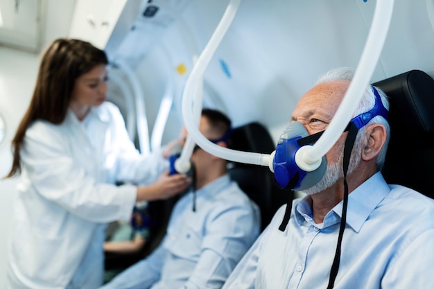 Uomo maturo che respira attraverso la maschera durante l'ossigenoterapia iperbarica in clinica