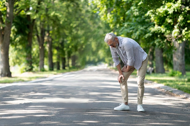 Uomo maturo che soffre di infortunio al ginocchio mentre cammina all'aperto nel parco