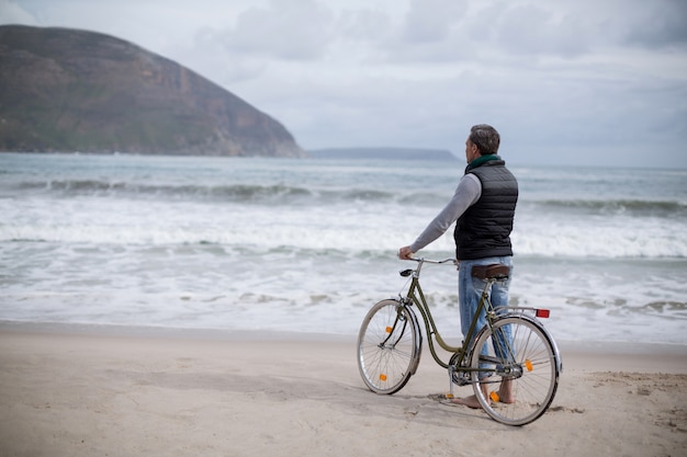 Uomo maturo che sta con la bicicletta sulla spiaggia