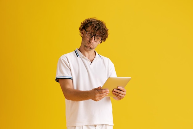 Uomo maturo con gli occhiali guardando il tablet con la faccia pensierosa contro lo sfondo giallo dello studio Brainstorming concetto di emozioni umane espressione facciale stile di vita gadget aziendali annuncio