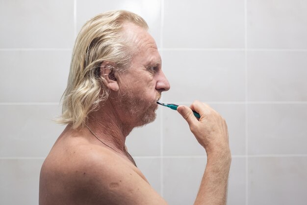Uomo maturo con la barba lunga si lava i denti in bagno Procedure di igiene mattutina