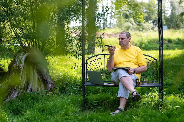 Uomo maturo con laptop e smartphone che lavora fuori nel concetto di home office verde giardino