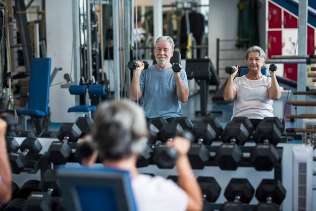 Uomo maturo con sua moglie che fa esercizio di bicipiti in palestra - concetto di fitness e stile di vita sano - allenare il loro corpo insieme - coppia di due anziani