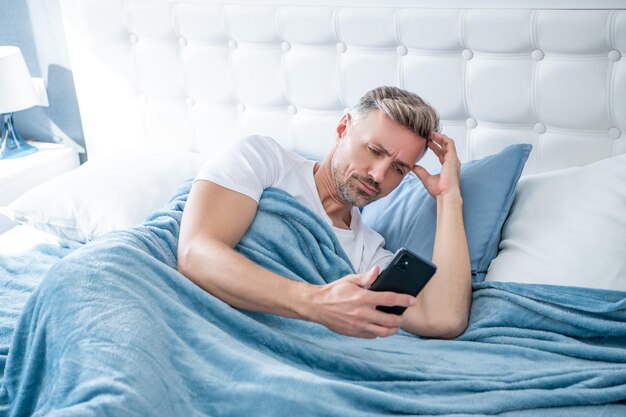 Uomo maturo confuso a letto che chiacchiera sul telefono