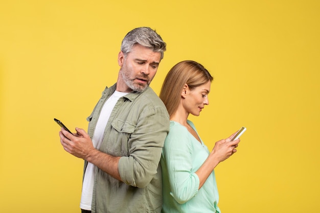 Uomo maturo curioso che prova a guardare la donna dello smartphone di sua moglie che tiene utilizzando gadget e chattando