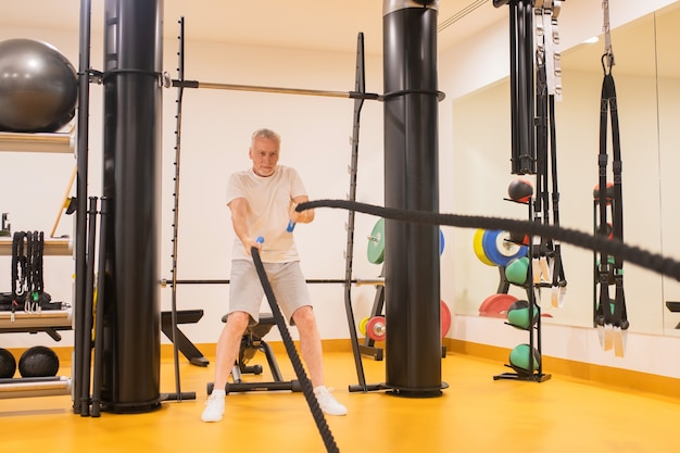 Uomo maturo in abiti sportivi che tira le corde in palestra