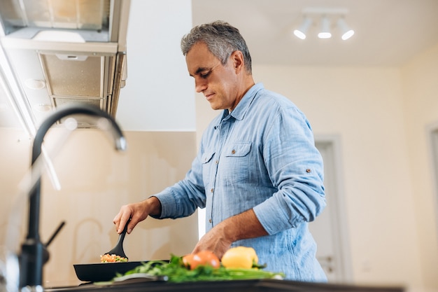 Uomo maturo in camicia blu che cucina sulla cucina moderna