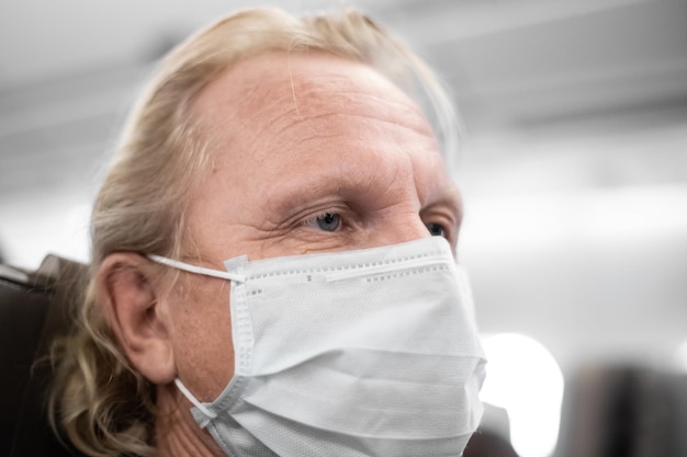 Uomo maturo in maschera medica con occhi stanchi e doloranti in cabina restrizioni di viaggio aereo coronavirus