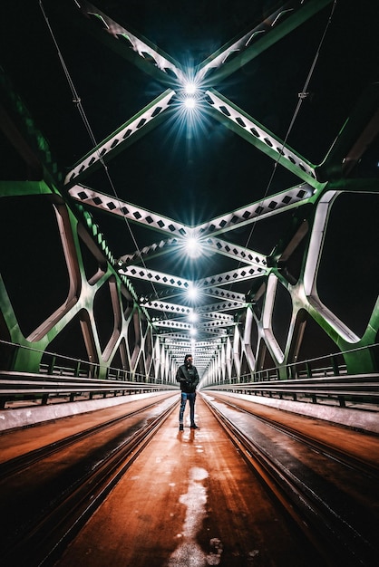 Uomo maturo in piedi su un ponte illuminato di notte