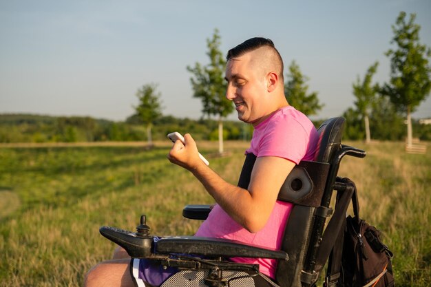 Uomo maturo in sedia a rotelle nera con in mano uno smartphone contro una persona in sedia a rotelle di sfondo rurale