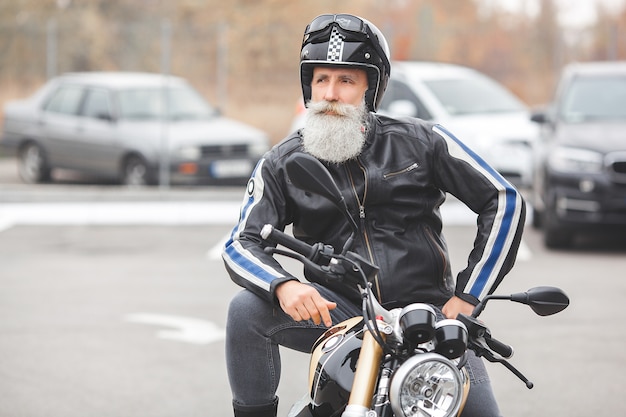 Uomo maturo in sella a una moto. Vecchio maschio in moto. Uomo barbuto all'aperto guida.