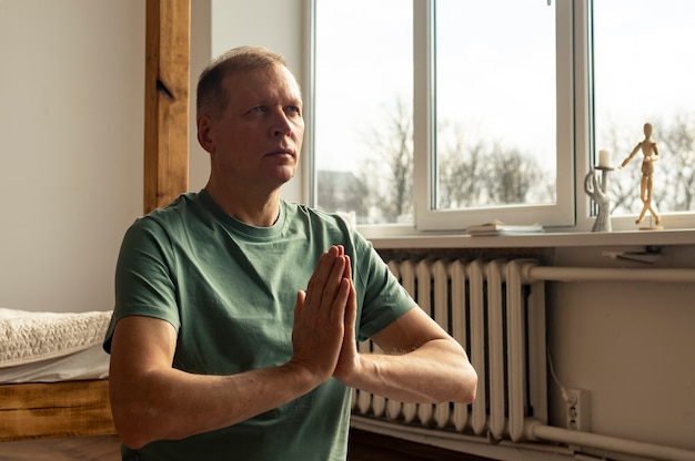 Uomo maturo meditando a casa accogliente con le mani che tengono insieme