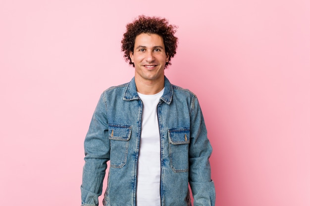 Uomo maturo riccio che indossa una giacca di jeans contro la parete rosa felice, sorridente e allegro.