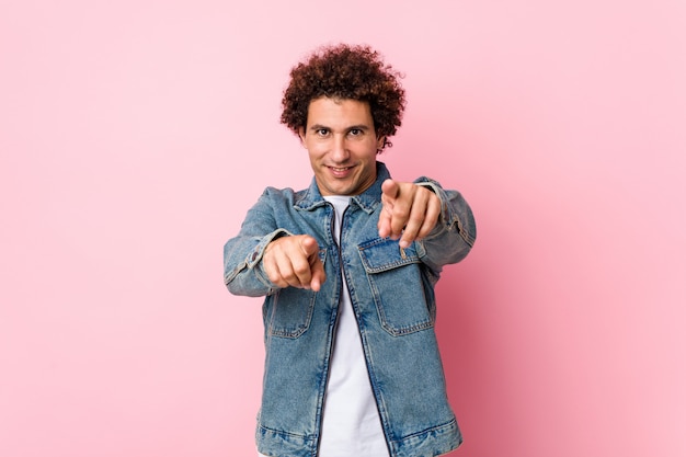 Uomo maturo riccio che indossa una giacca di jeans su sfondo rosa sorrisi allegri che punta verso la parte anteriore.