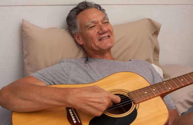 Uomo maturo sdraiato a letto a suonare la chitarra.