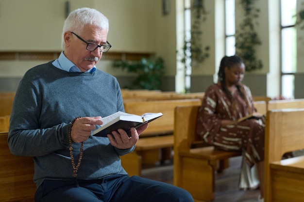 Uomo maturo serio in abbigliamento casual che guarda attraverso i versetti del vangelo in chiesa