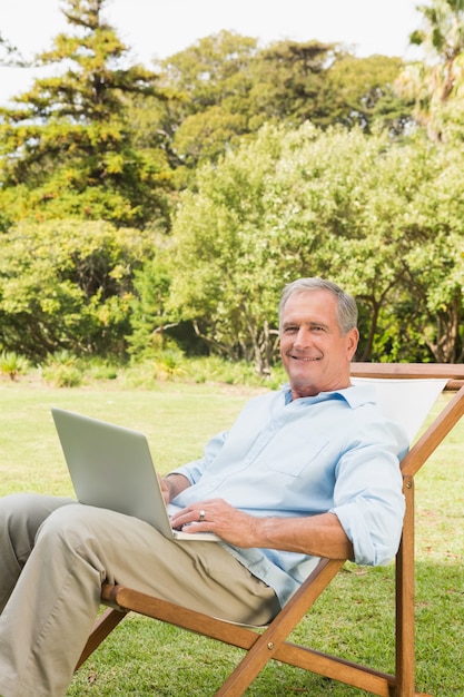 Uomo maturo sorridente che per mezzo del computer portatile