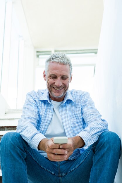 Uomo maturo sorridente che per mezzo dello smartphone a casa