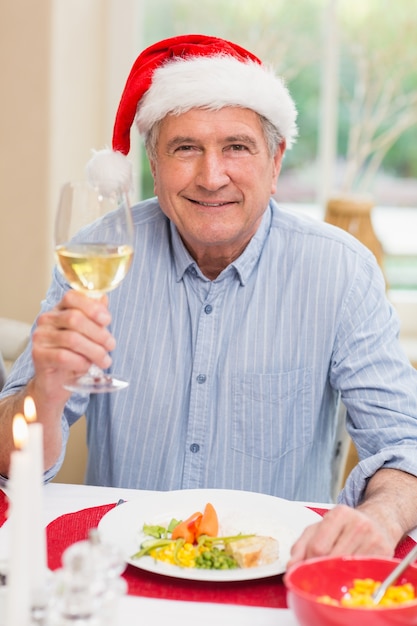 Uomo maturo sorridente in cappello della santa che tosta con il vino bianco