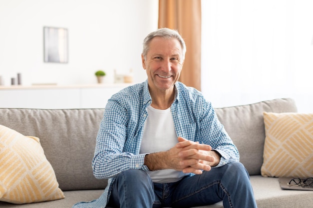 Uomo maturo sorridente seduto sul divano e in posa