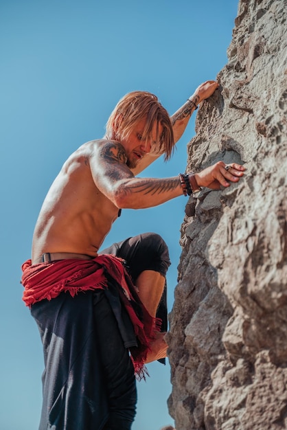 Uomo maturo tatuato che tiene la spada pronta a combattere e arrampicarsi sulla roccia con sfondo blu