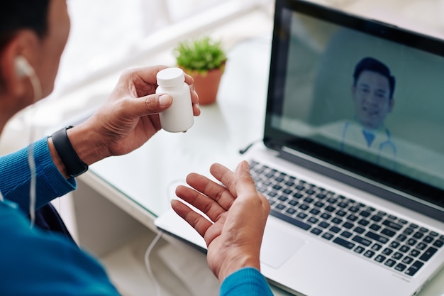 Uomo maturo videochiamata medico e chiedendo quale medicina, vitamine e integratori dovrebbe prendere