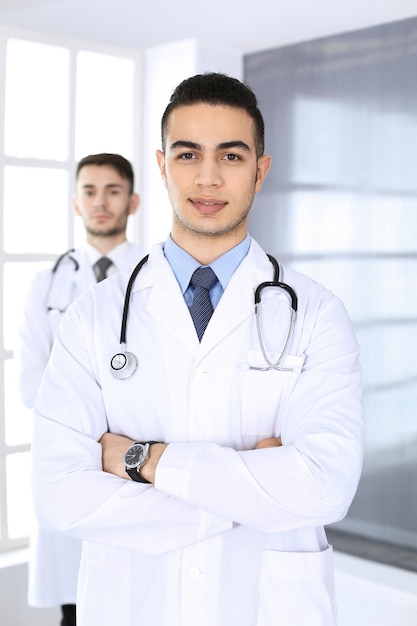 Uomo medico arabo in piedi con un collega caucasico in studio medico o clinica Diversi medici team di medicina e concetto di assistenza sanitaria