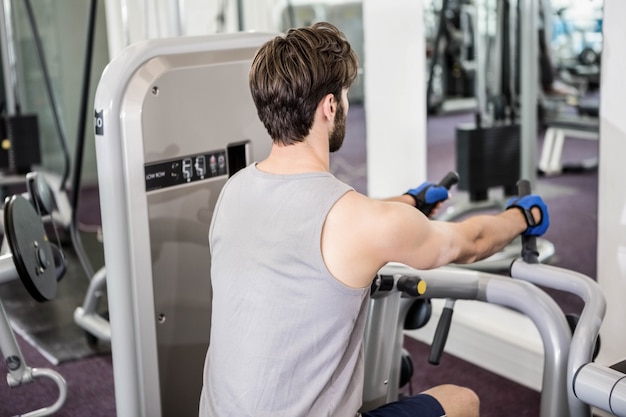 Uomo messo a fuoco usando la macchina dei pesi per le armi alla palestra