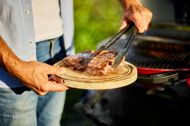 Uomo messo giù su una tavola di legno pronto da mangiare bistecca alla griglia carne maschio bistecca arrosto carne sul grill a gas sul barbecue grill all'aperto nel cortile estate picnic in famiglia cibo sulla natura