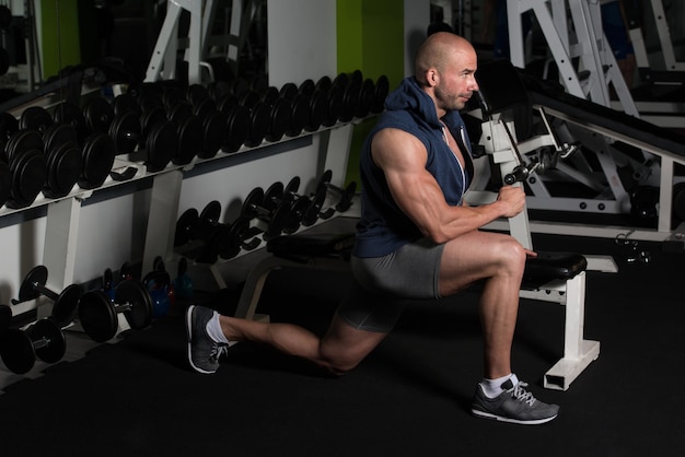 Uomo muscolare che allunga la gamba sul pavimento in una palestra e flette i muscoli Modello di fitness bodybuilder atletico muscolare