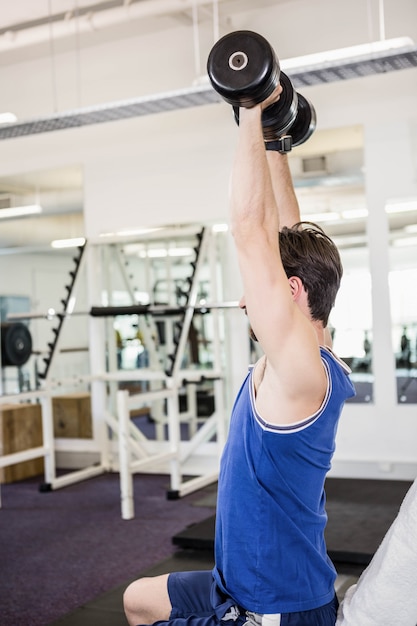 Uomo muscolare che alza i dumbbells sul banco in palestra