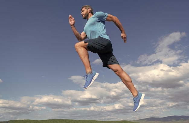 Uomo muscolare che corre in abbigliamento sportivo all'aperto sulla sfida del fondo del cielo