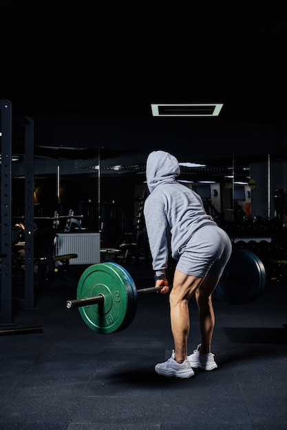 Uomo muscolare che fa esercizio di stacco con bilanciere in palestra