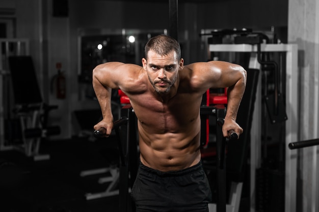 Uomo muscolare che fa i piegamenti sulle barre irregolari nella palestra del crossfit.