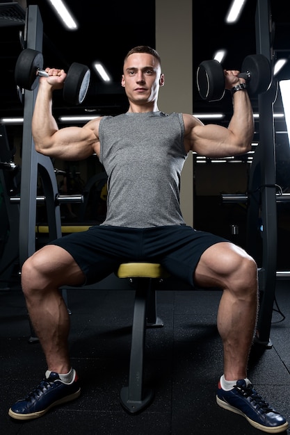 Uomo muscolare che fa pressa sopraelevata con manubri in palestra.