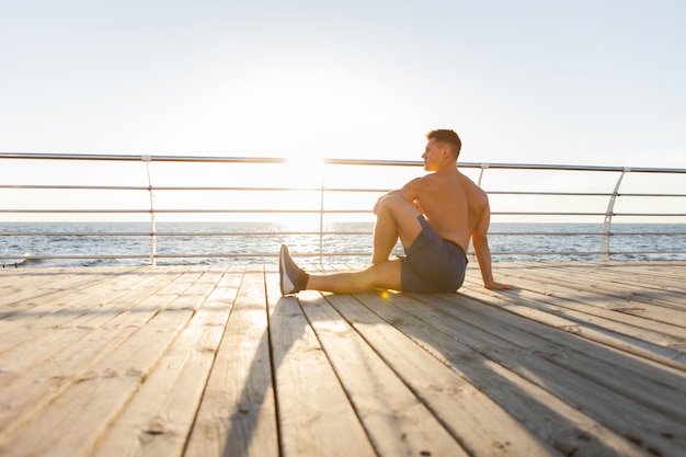 Uomo muscolare che pratica asana yoga pone per allungare i muscoli all'alba sulla spiaggia