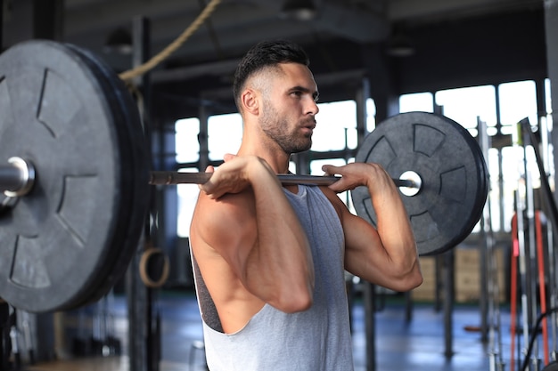 Uomo muscolare che si allena in palestra facendo esercizi con bilanciere al bicipite.