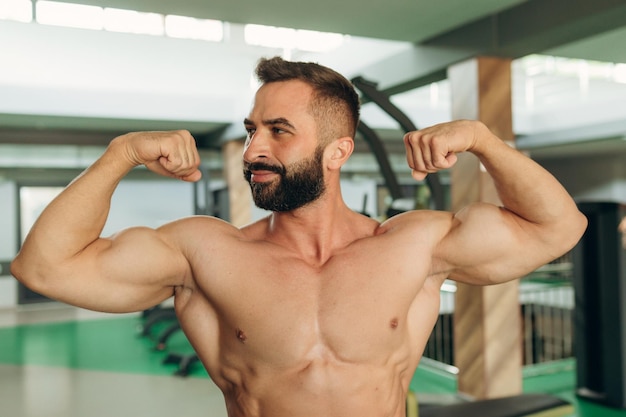 Uomo muscolare in palestra Gli uomini fitness con il torso nudo mostrano i suoi bicipiti
