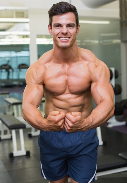 Uomo muscolare senza camicia che flette i muscoli in palestra