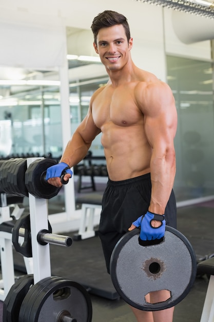 Uomo muscolare senza camicia che solleva peso in palestra