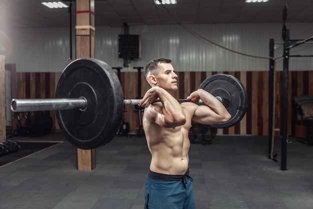 Uomo muscoloso atletico che si esercita con un bilanciere pesante in un moderno centro benessere. Bodybuilding e Fitness