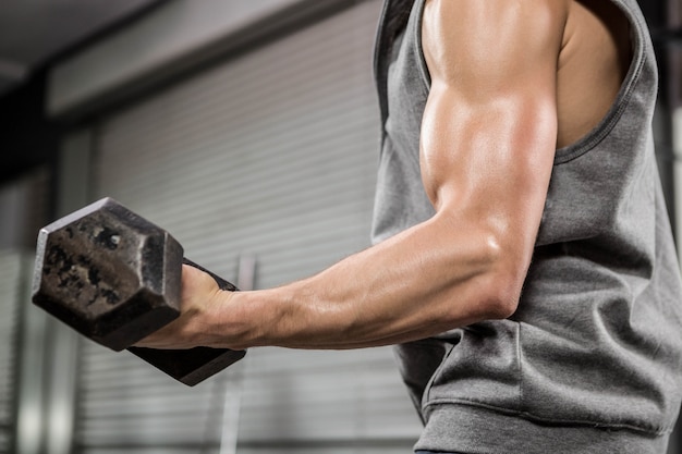 Uomo muscoloso con ponticello grigio che alza dumbbell a thegym