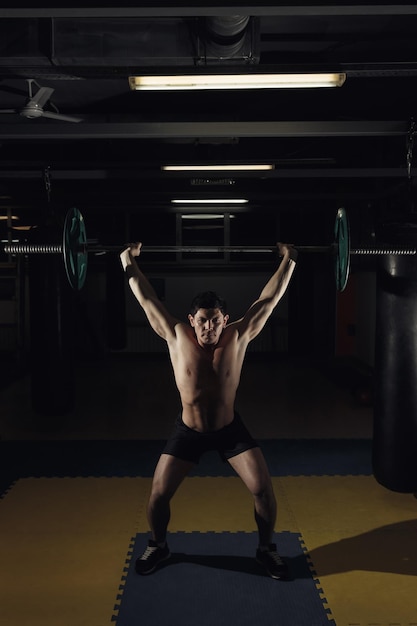 Uomo muscoloso in una palestra di crossfit che solleva un bilanciere.