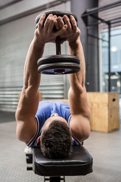 Uomo muscoloso sulla panca sollevamento manubri presso la palestra di crossfit