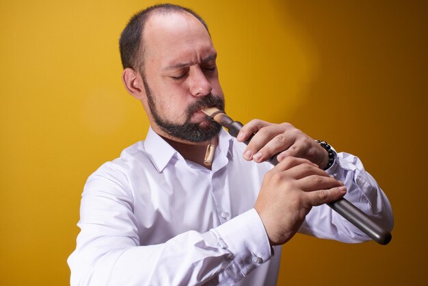 Uomo musicista professionista che gioca un primo piano del tubo in uno studio giallo. Strumento a fiato popolare, flauto