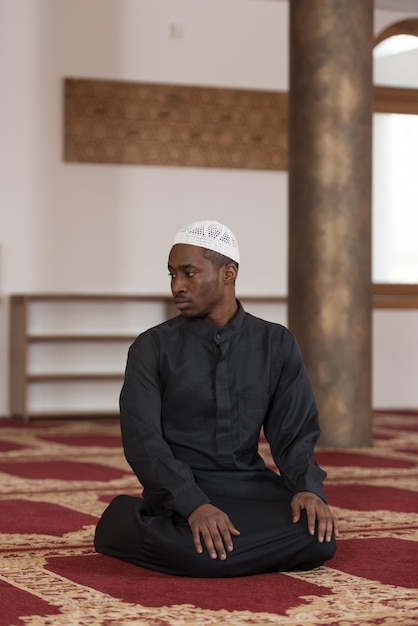 Uomo musulmano africano che fa la tradizionale preghiera a Dio mentre indossa un cappello tradizionale Dishdasha